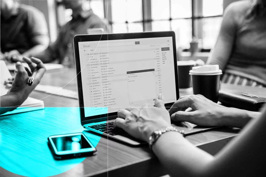 Employee reviews email messages on a laptop while working with colleagues