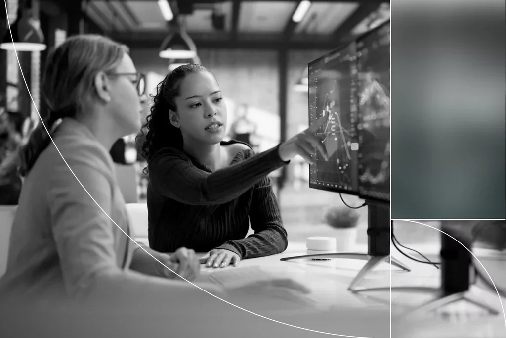 Two professionals reviewing financial data and charts on a computer monitor.