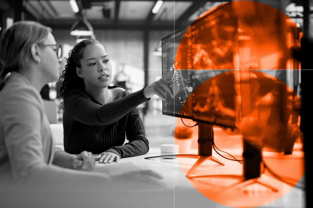 Two professionals reviewing data and performance trends on a computer monitor
