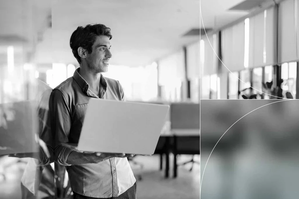 Professional carries a laptop through a modern office workspace.