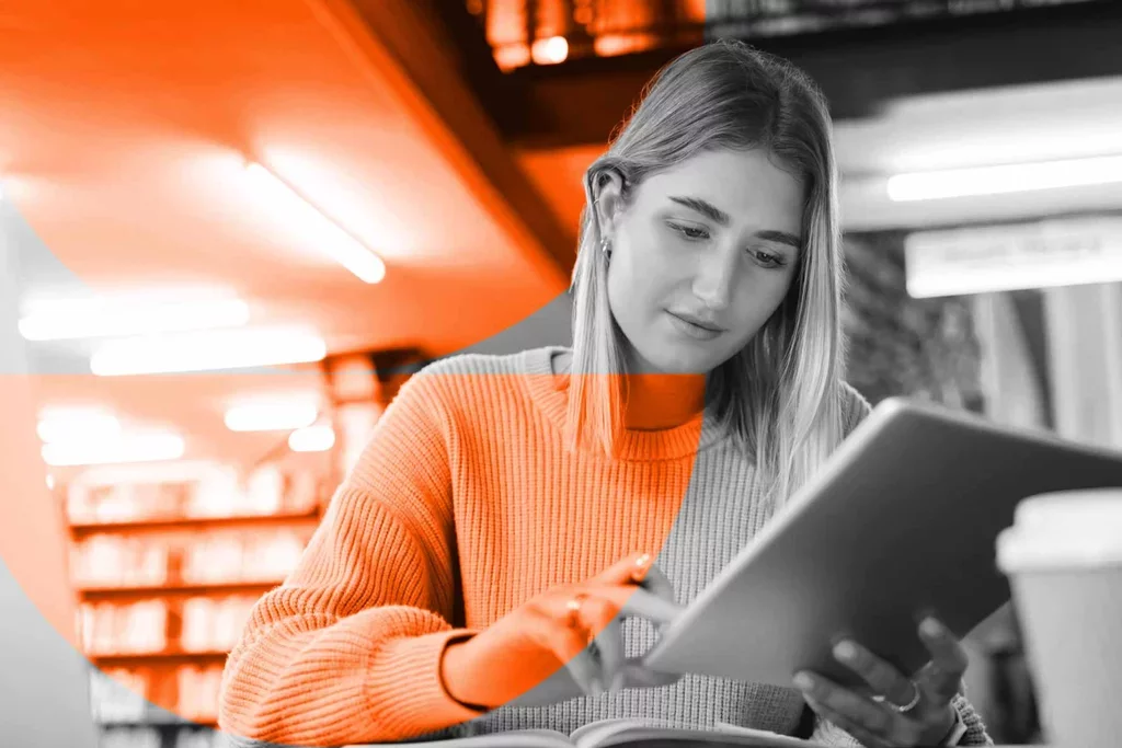 Student uses a tablet while studying at a desk in a library