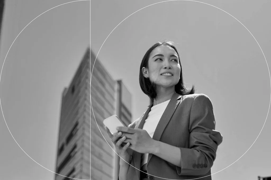 Business professional holding a smartphone outside an office building.