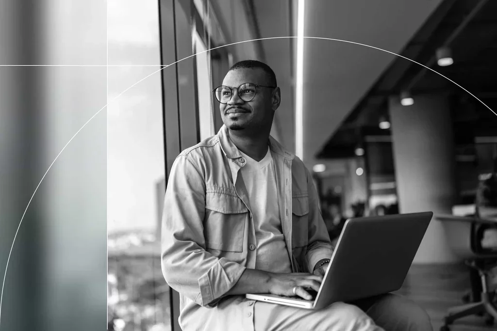 Business professional working on a laptop beside an office window.