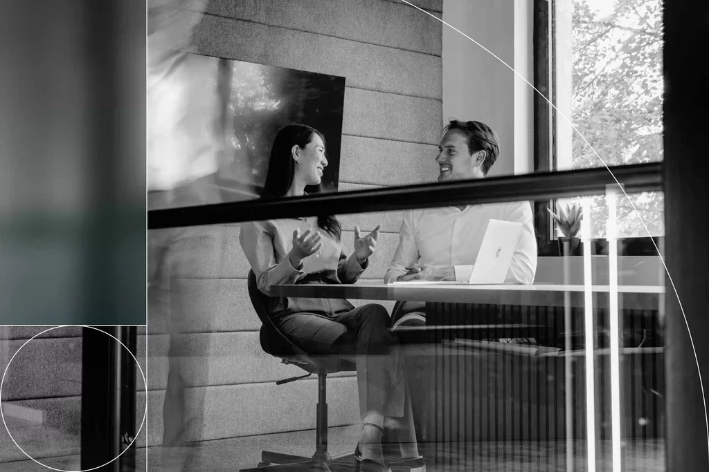 Two colleagues discussing their work together at a laptop in a meeting room.