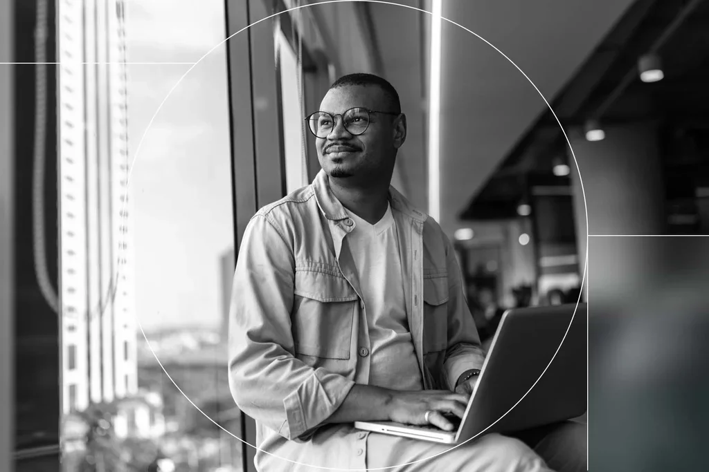 Professional using a laptop while working near a window in a modern office.