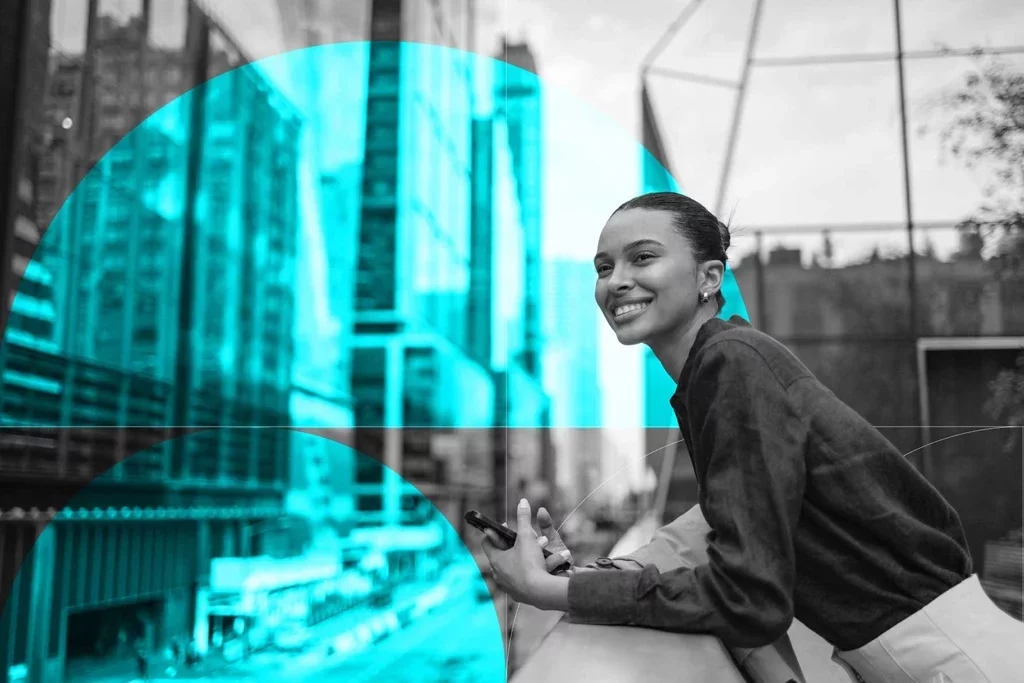 Business professional smiling while holding a smartphone in an urban setting.