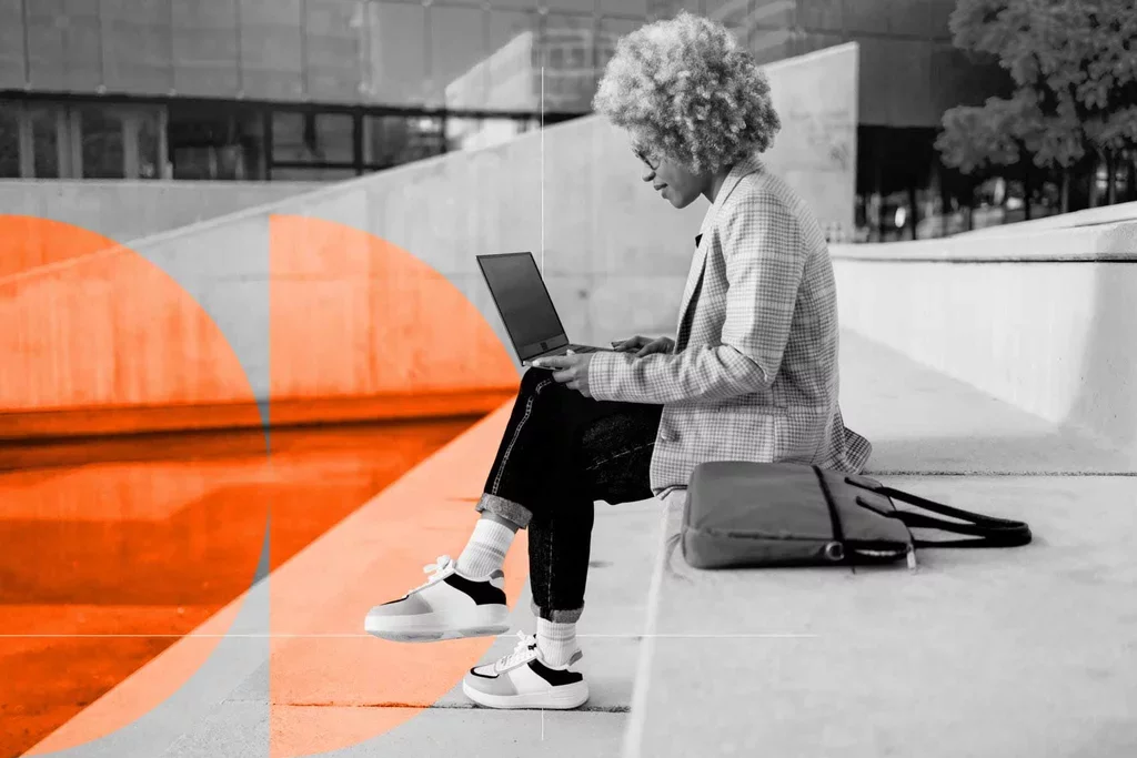Professional seated outdoors using a laptop with a work bag beside them.