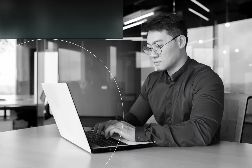 Business professional wearing glasses and working on a laptop at a desk in a modern office.