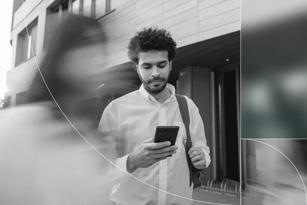 Business professional checking his smartphone outside an office building as people walk past.