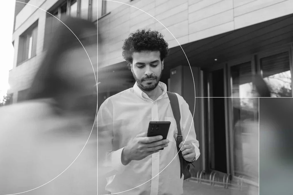 Professional checks a smartphone while walking outside an office building.