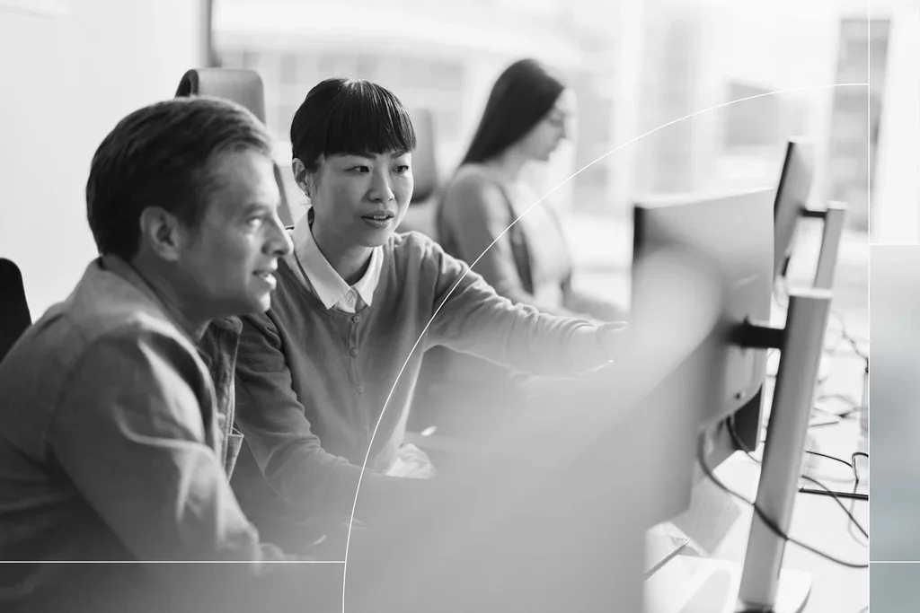 Two cybersecurity professionals reviewing information together on desktop monitors.