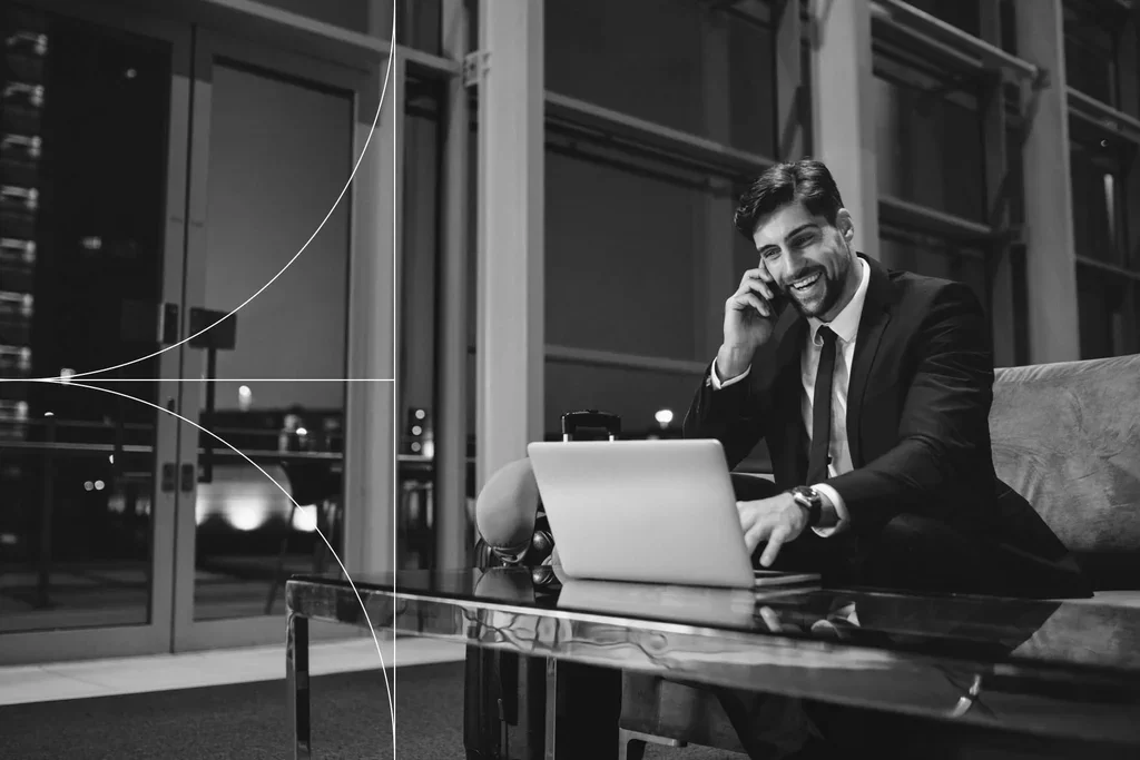 Business professional using a laptop while speaking on a smartphone.