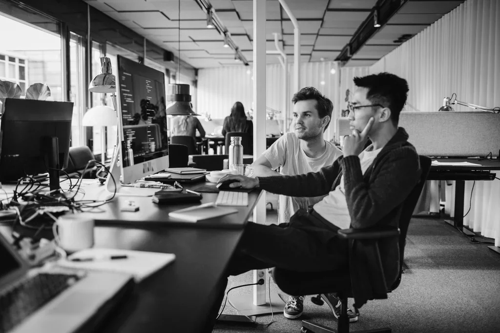 two people sitting around a computer monitor thinking 