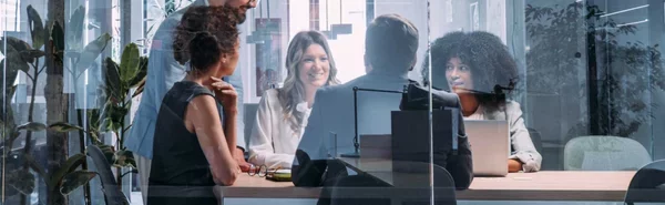A diverse team of security and IT leaders meeting in a glass conference room, collaborating around a table with laptops—symbolizing full accountability and governance across AI and enterprise security initiatives at Proofpoint.