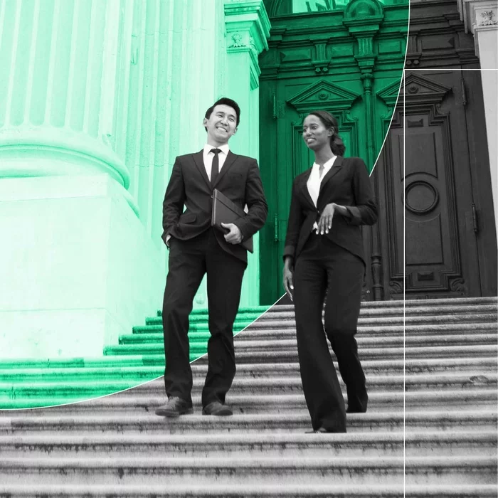Two government professionals walking down courthouse steps while carrying documents.