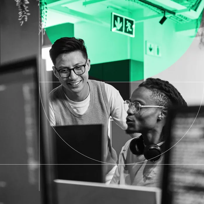 Two colleagues collaborate while reviewing information on computer monitors.