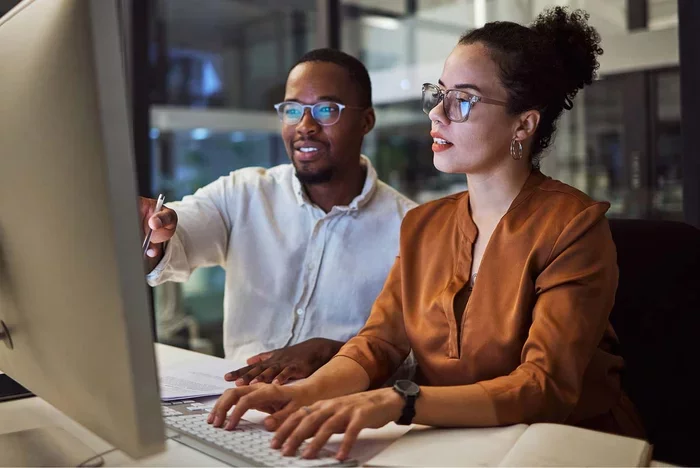 Colleagues reviewing information together on desktop computer in office.