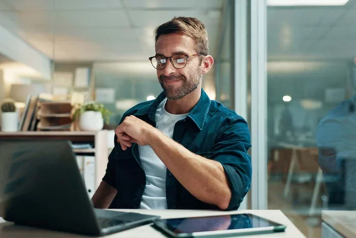 Professional smiling while using laptop during online training session.
