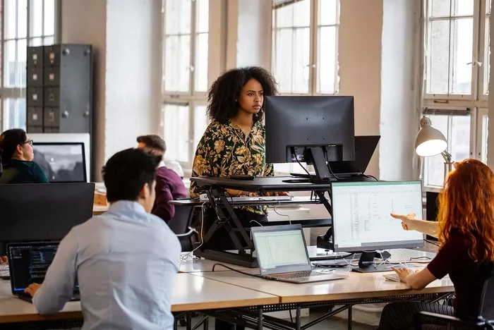 Team monitoring data on multiple screens in open office workspace.