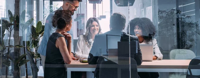 A diverse team of security and IT leaders meeting in a glass conference room, collaborating around a table with laptops—symbolizing full accountability and governance across AI and enterprise security initiatives at Proofpoint.