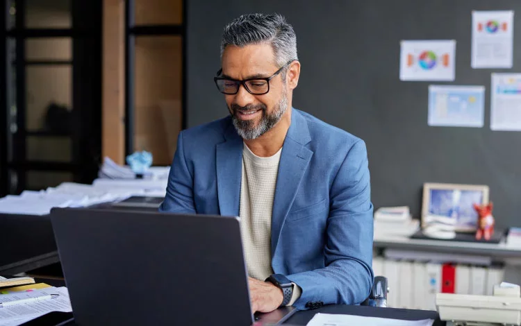 Man using laptop at desk analyzing information and reports.