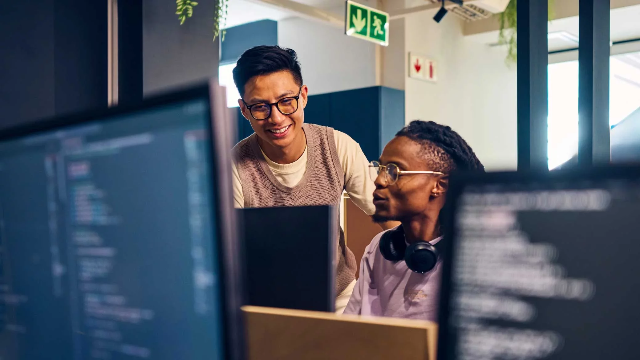 Two security engineers collaborating at a workstation, reviewing code and system activity on multiple monitors—reflecting Proofpoint teams deploying and managing secure enterprise solutions.