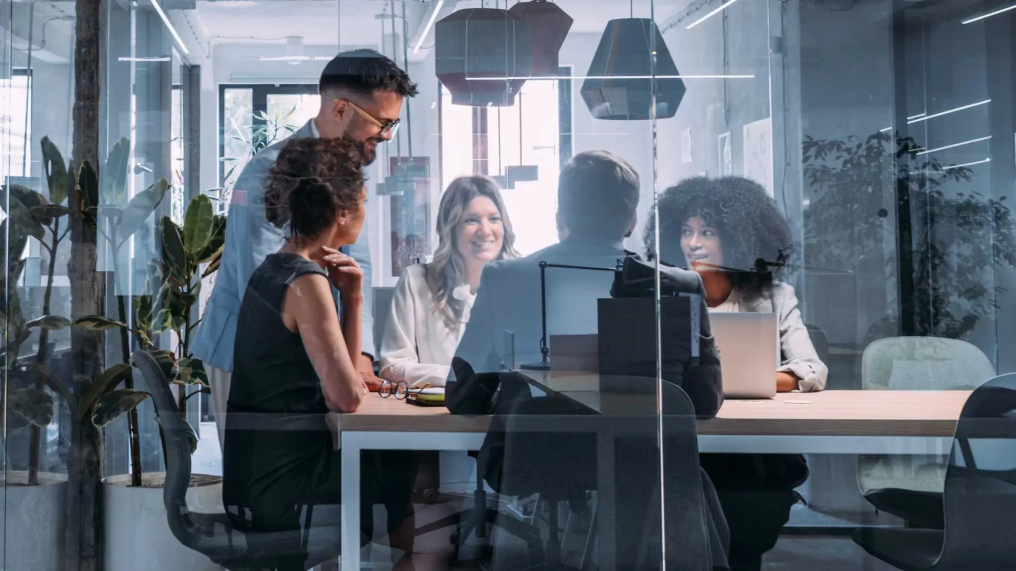 A diverse team of security and IT leaders meeting in a glass conference room, collaborating around a table with laptops—symbolizing full accountability and governance across AI and enterprise security initiatives at Proofpoint.