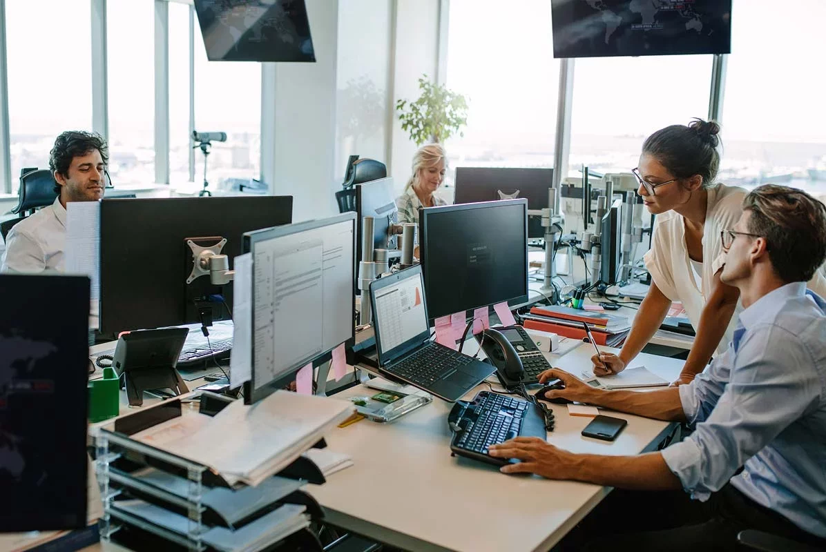 IT team collaborating at workstations and monitoring systems in office.