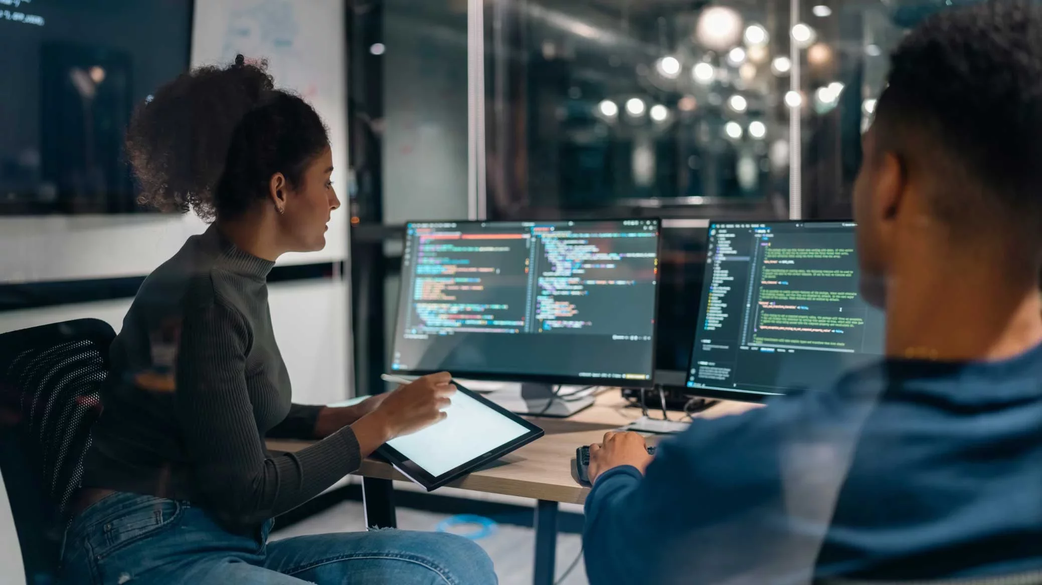 Two engineers collaborating at workstation with multiple code screens.