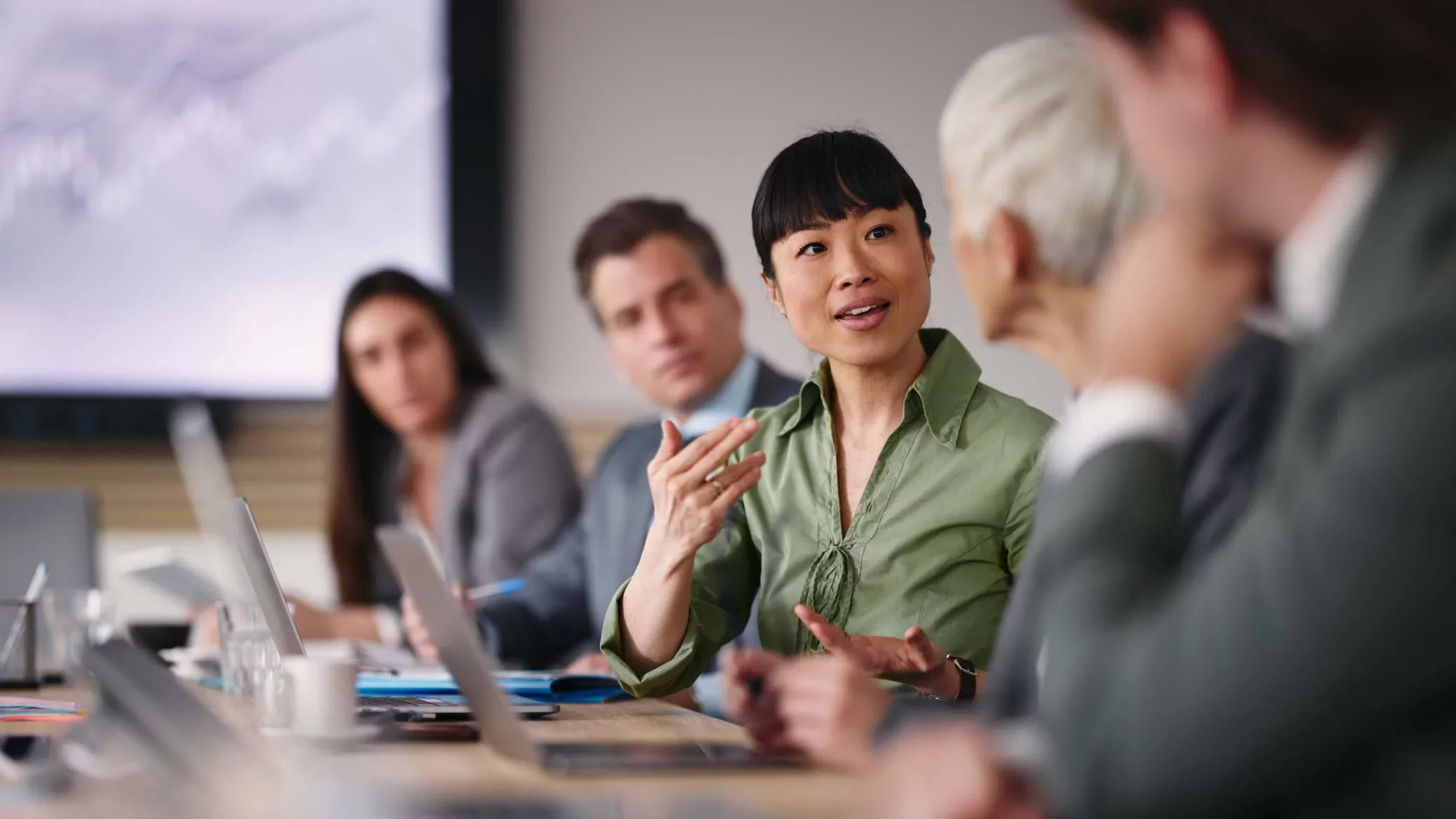 Business leaders collaborating in a conference room around a laptop, reviewing dashboards and strategy—representing secure acceleration of enterprise AI adoption with Proofpoint.