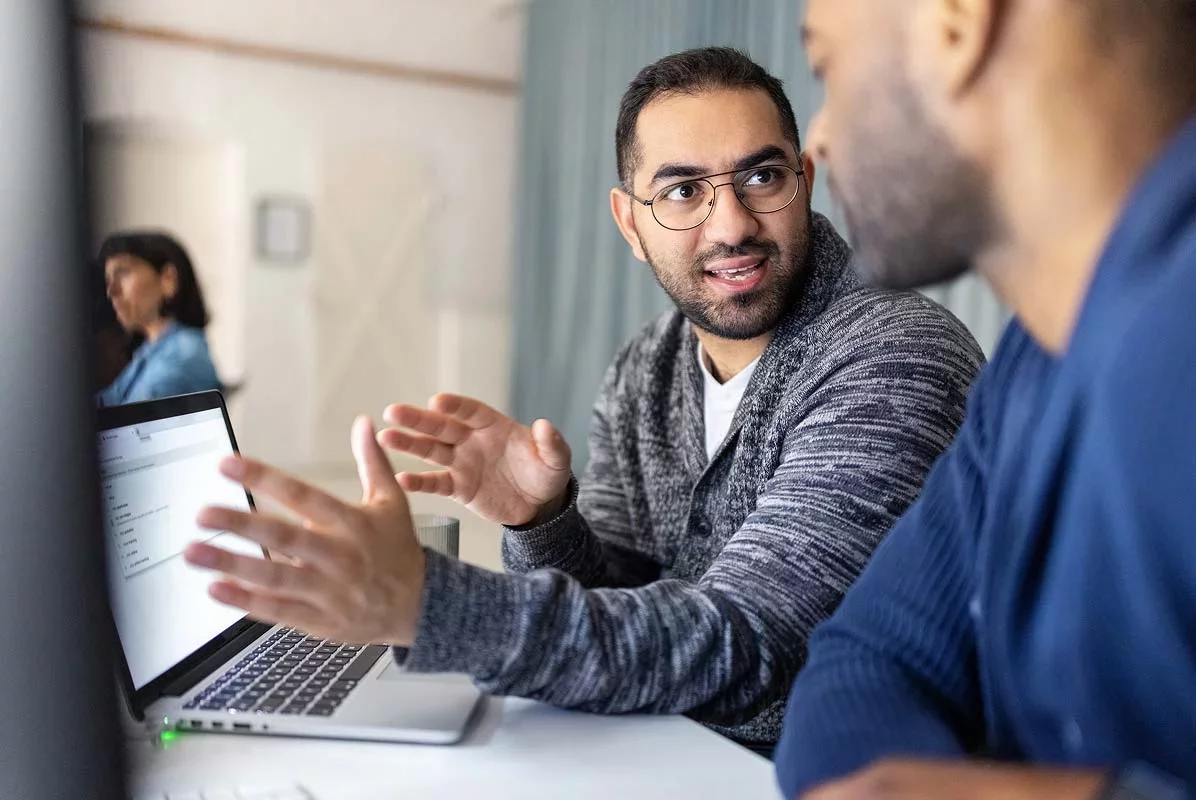 Two colleagues discussing data while reviewing laptop screen together.