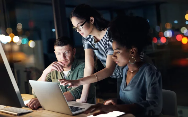 Three cybersecurity professionals collaborating around a laptop in a modern office, analyzing data on screen—framed by a green curved graphic on a black background consistent with Proofpoint branding.