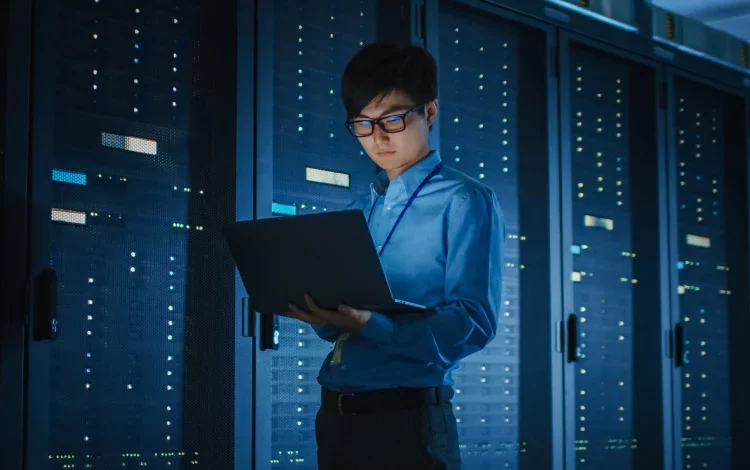 A security analyst working on a laptop inside a data center, reviewing enterprise AI governance and security controls—framed by a green curved graphic on a black background in Proofpoint brand style.