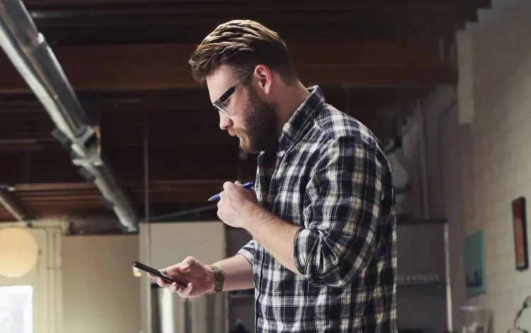 Professional reviewing smartphone while holding pen in office.