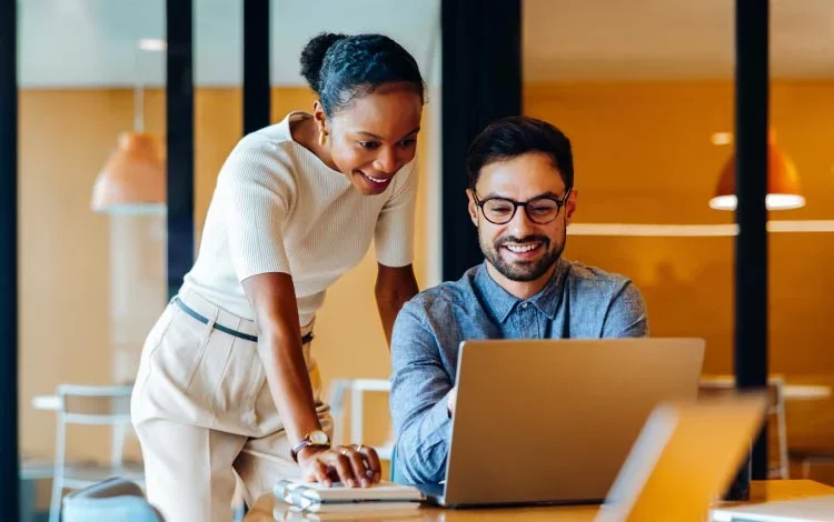 Colleagues working together on laptop analyzing information at desk.